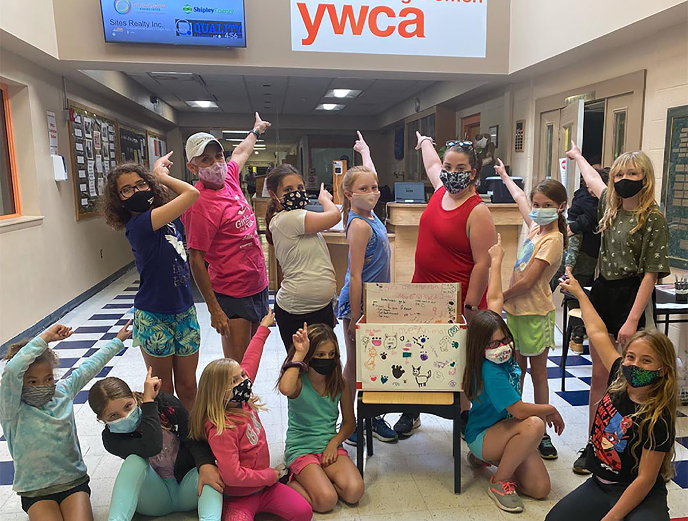 Group of women and kids with masks on pointing to the YWCA sign.